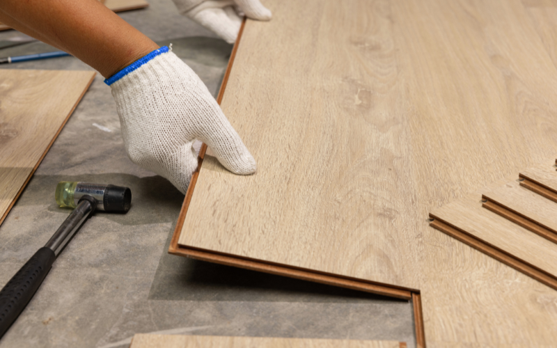 Mano de instalador con guante blanco colocando tabla de suelo laminado o parquet flotante con sistema clic, mostrando el método de instalación de suelos en reformas de Barcelona y Tarragona